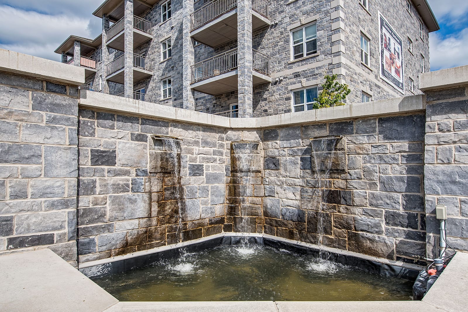 Three-spout water feature set into a limestone wall at the front of the building